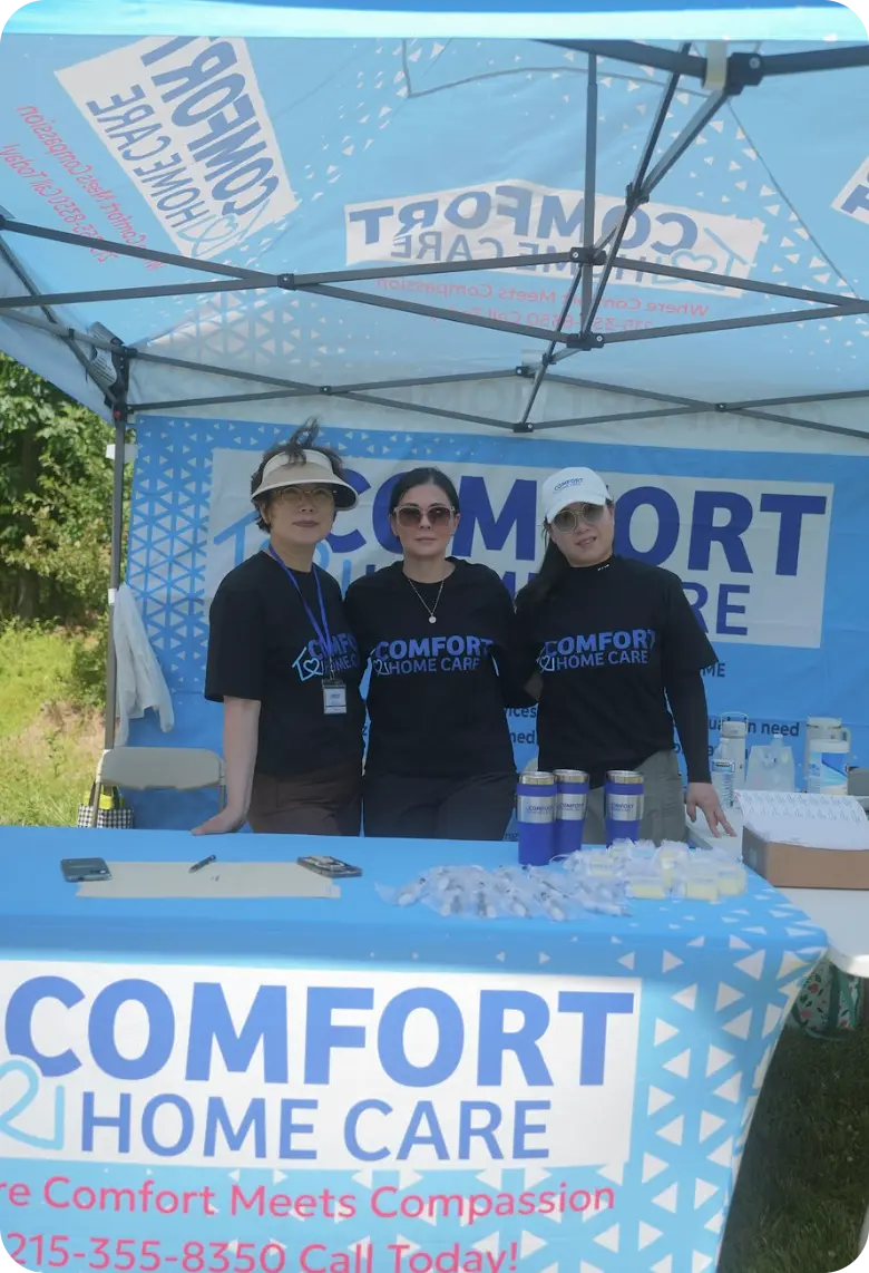 Comfort Home Care Team at Community Outreach Event | Comfort Home Care Three Comfort Home Care team members standing at a branded community outreach event booth