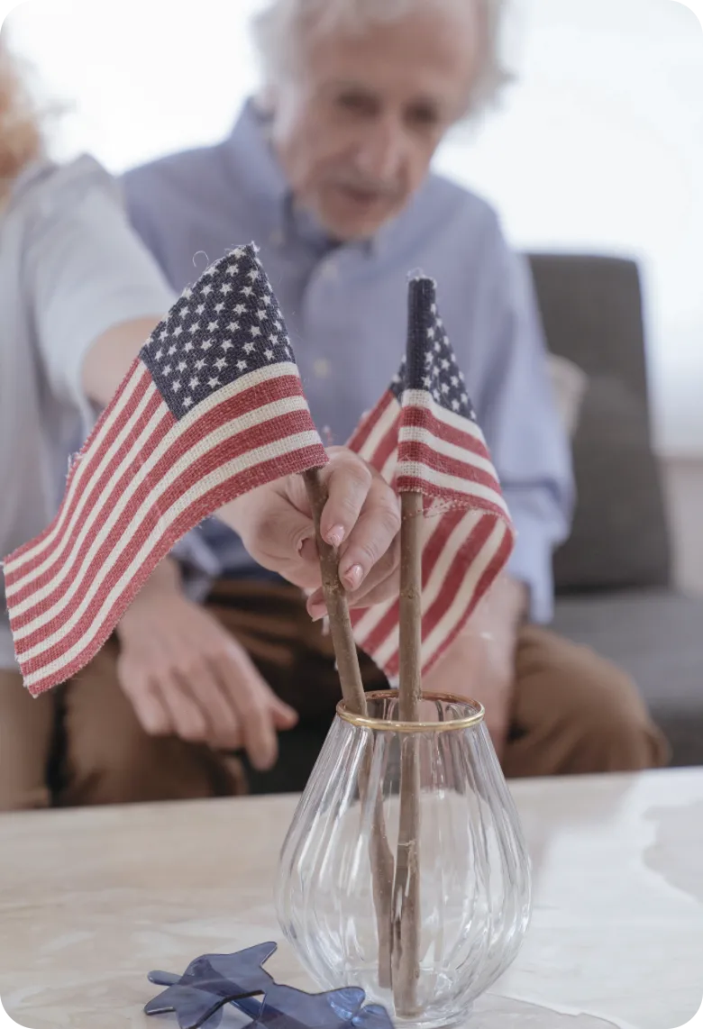 Senior Couple Displaying American Flags at Home | Comfort Home Care Senior couple arranging American flags in a vase at home